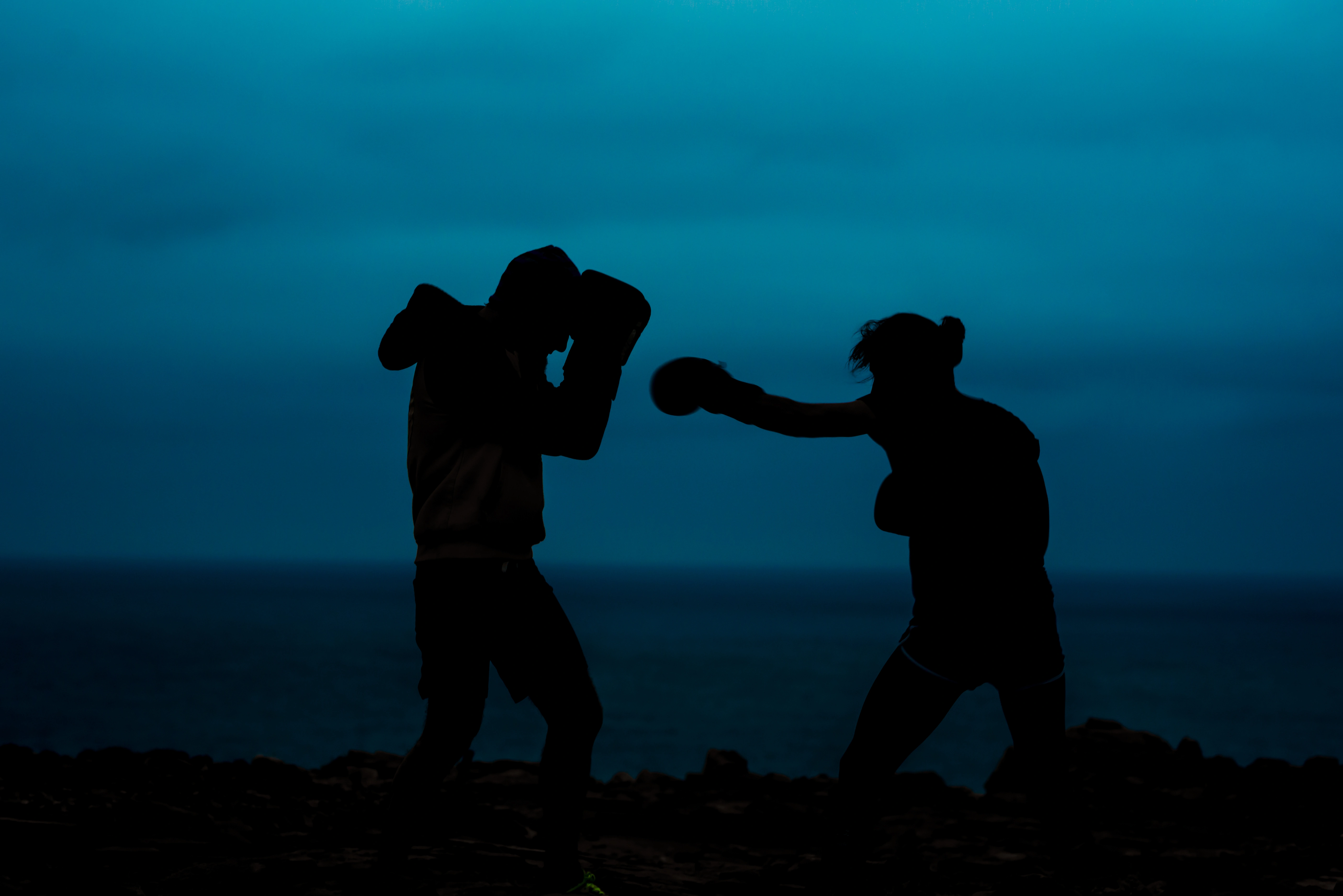 Silhouetted boxers training and sparring near the ocean at night